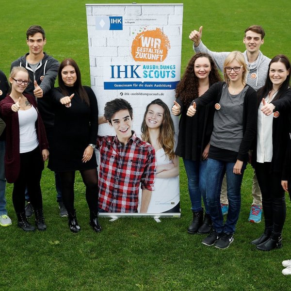Viele Personen stehen vor einem Aufsteller und zeigen mit dem Daumen hoch