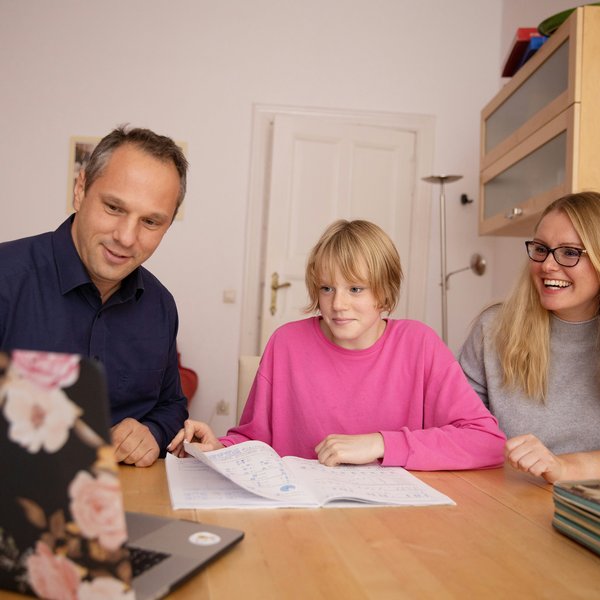 Vater und Mutter mit Kind vor Laptop, unterstützend bei der Berufsorientierung. 