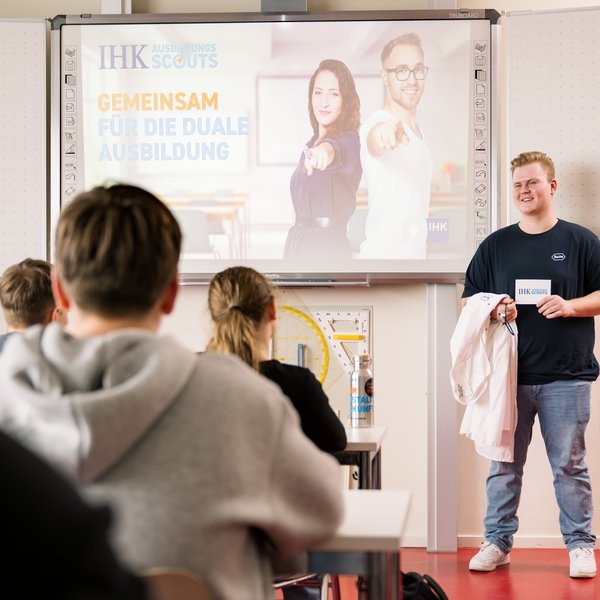 Ein Azubi steht vor der Schulklasse und berichtet von seiner Ausbildung.