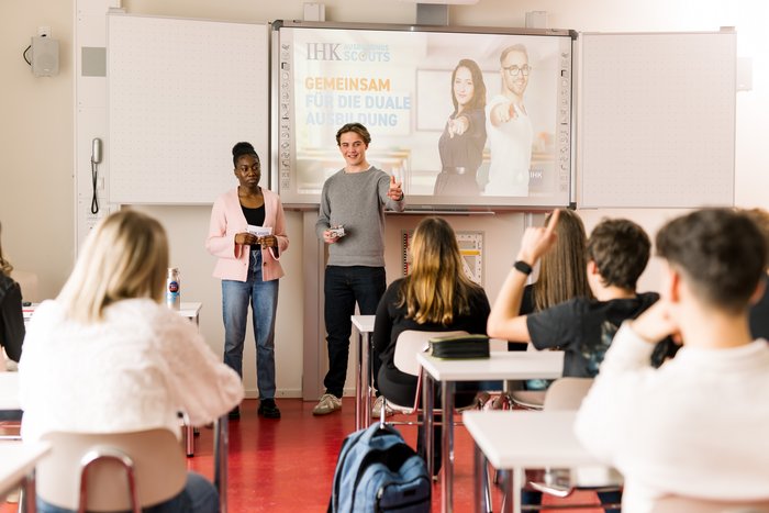 Zwei Auszubildende erklären ihre Ausbildung vor einer Schulklasse