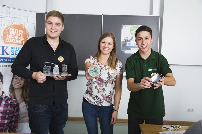 3 Azubis halten Alltagsgegenstände ihrer Ausbildung in die Kamera. 